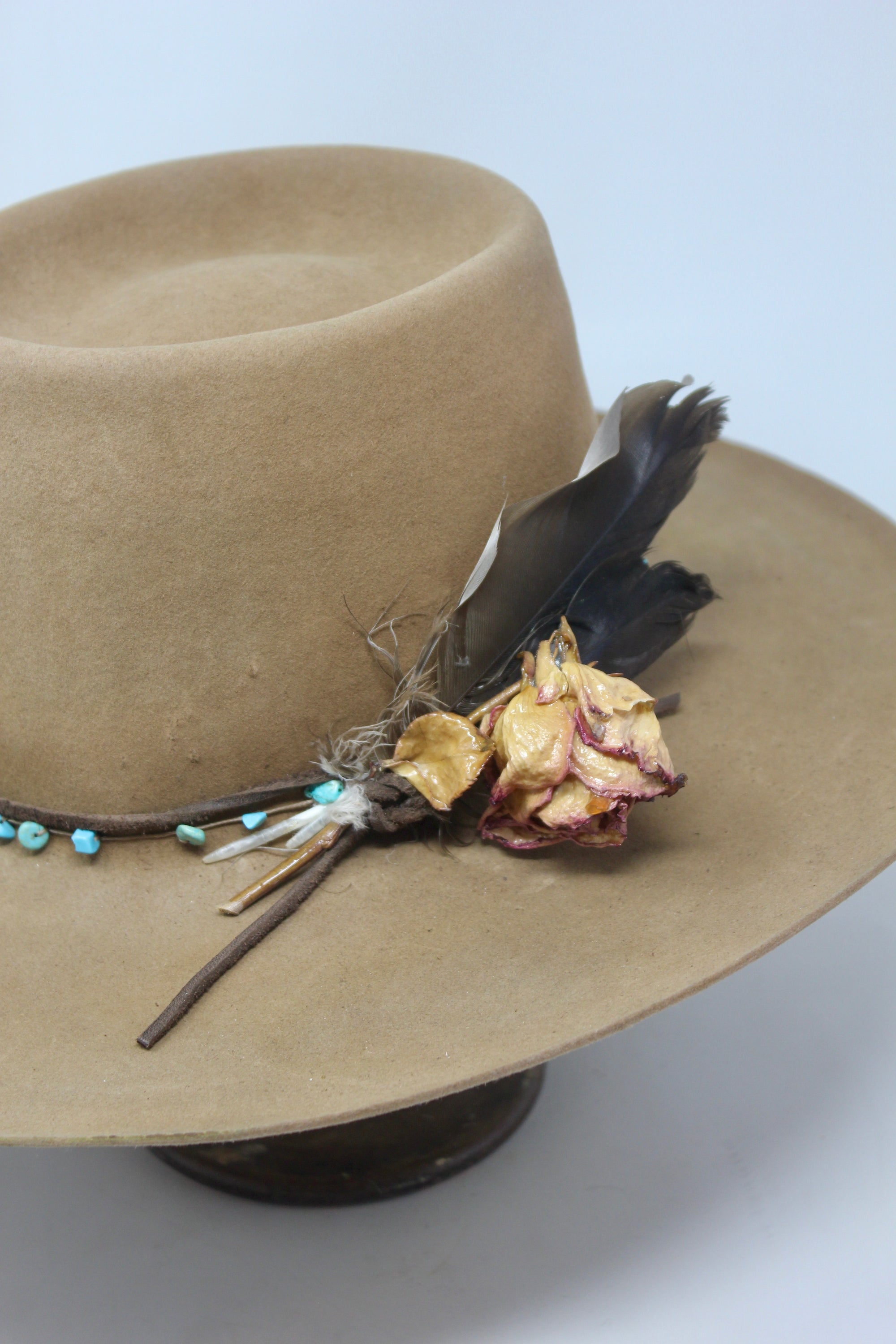 close up of the Tele Top Camel hat by Lone Hawk Hats featuring a dipped telescope crown, wider brim, hand-knotted turquoise band, sterling hawk pin, and found feather accent.