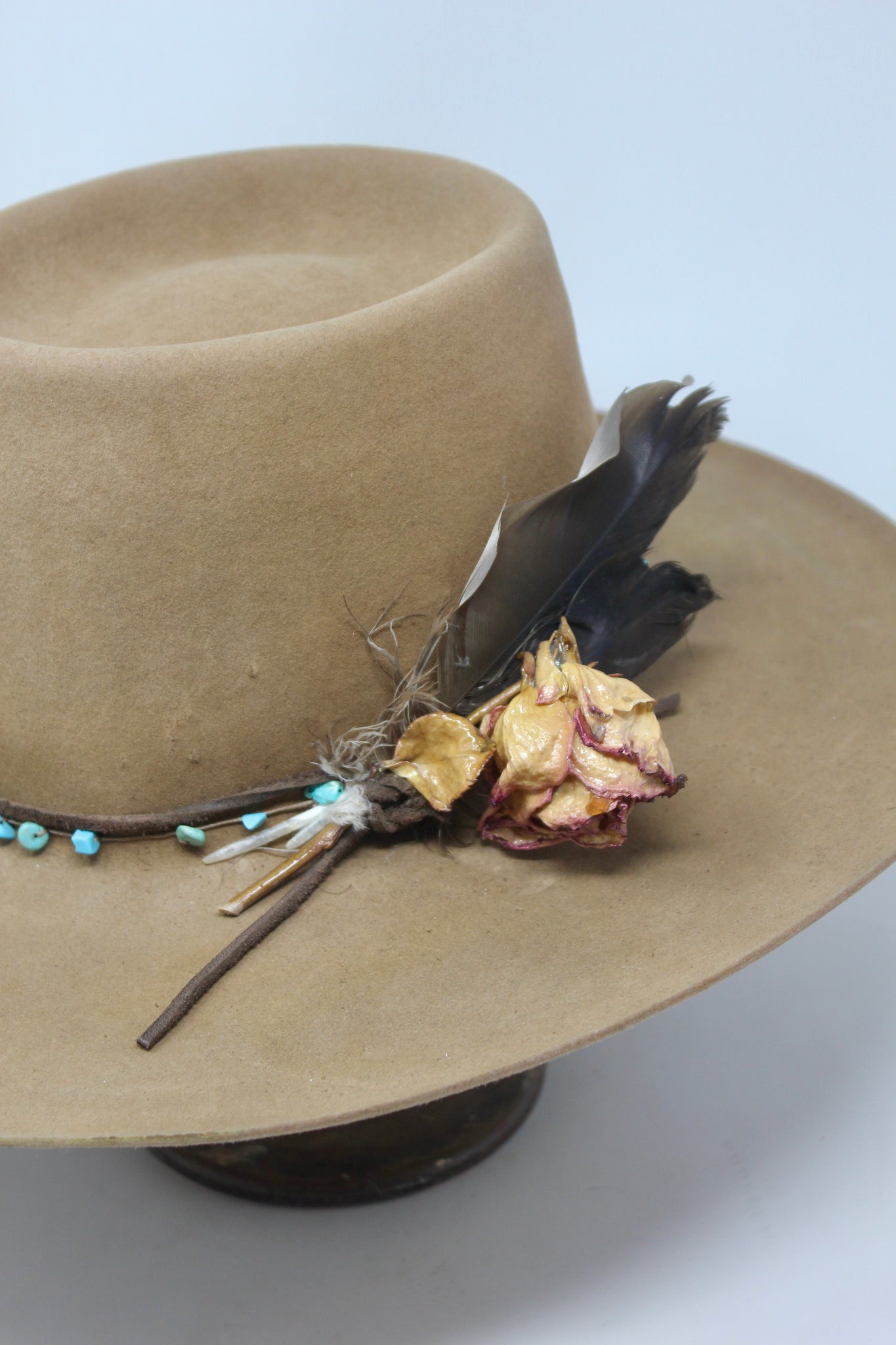 close up of the Tele Top Camel hat by Lone Hawk Hats featuring a dipped telescope crown, wider brim, hand-knotted turquoise band, sterling hawk pin, and found feather accent.