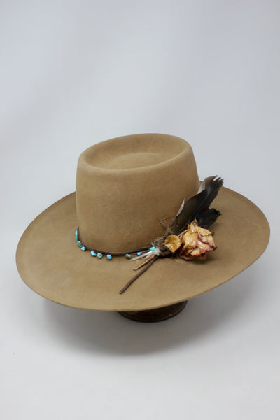 Left view of the Tele Top Camel hat by Lone Hawk Hats featuring a dipped telescope crown, wider brim, hand-knotted turquoise band, sterling hawk pin, and found feather accent.