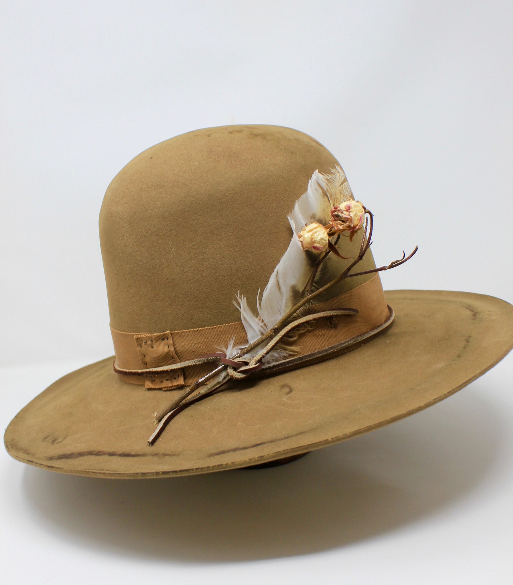 left view of the Cree Mountain hat by Lone Hawk Hats featuring a tall open crown, flat brim with a slight pencil roll, hand-sewn band, feather accents, and light distressing.