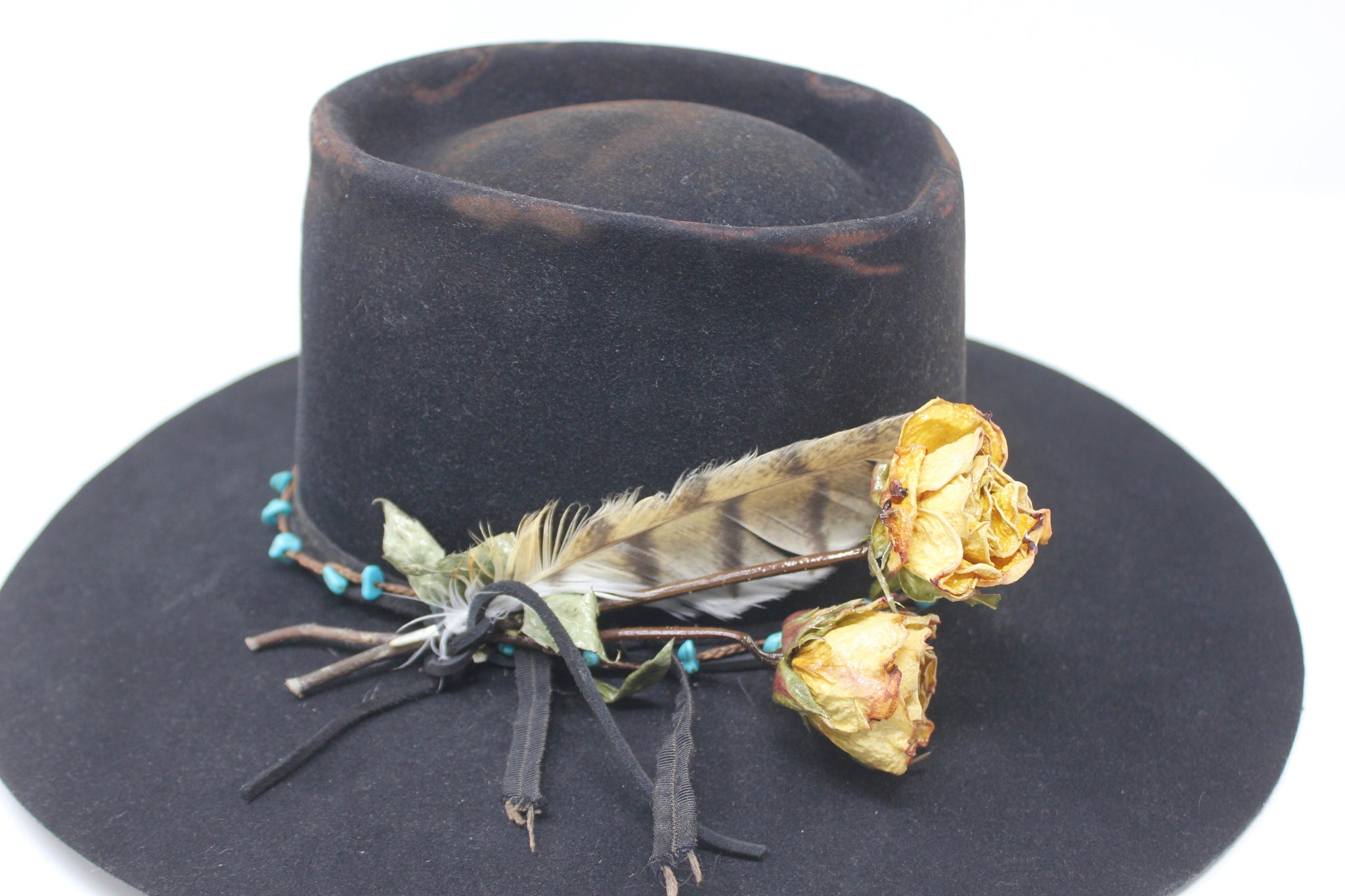 Close up view of the turquoise embellishment, and found feather detail on The Horse Thief Badlands custom Lone Hawk hat featuring a distressed telescope crown, wide flat brim, handcrafted in California.