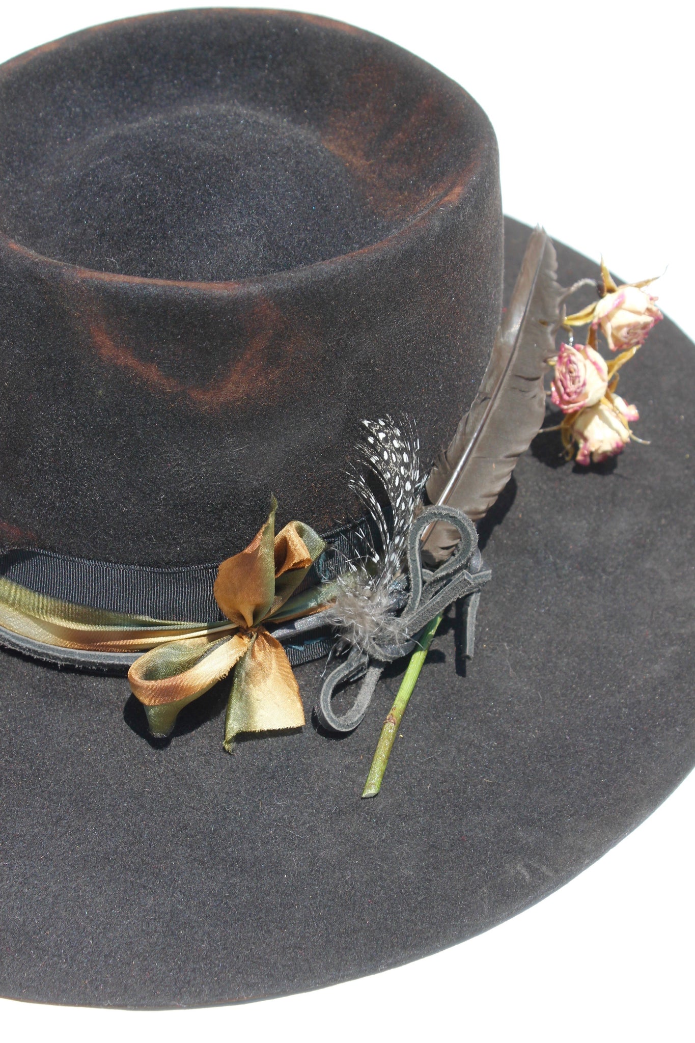 close up of hand-dyed silk ribbon, dried flowers, and found feathers on The Emerald Hawk by Lone Hawk Hats, a distressed telescope crown western hat featuring a wide flat brim with Bardot dip.