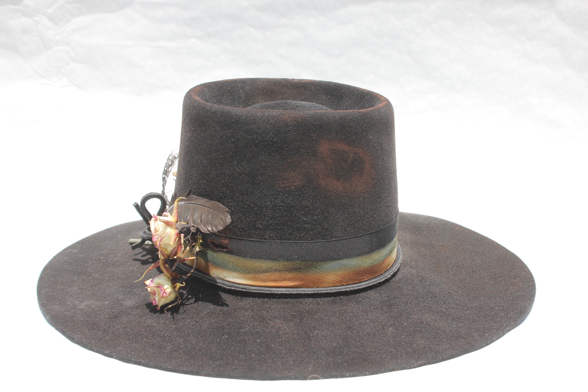 back view of The Emerald Hawk by Lone Hawk Hats, a distressed telescope crown western hat featuring a wide flat brim with Bardot dip, hand-dyed silk ribbon, dried flowers, and found feathers.