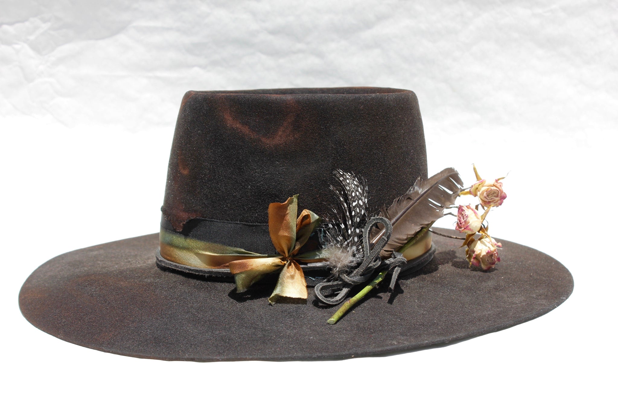 left view of The Emerald Hawk by Lone Hawk Hats, a distressed telescope crown western hat featuring a wide flat brim with Bardot dip, hand-dyed silk ribbon, dried flowers, and found feathers.