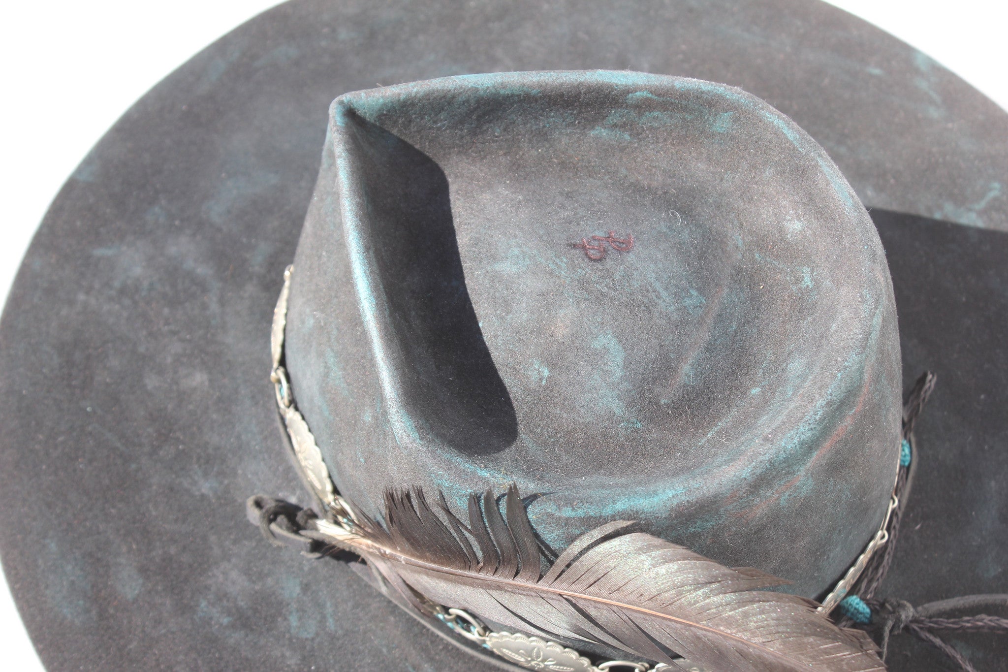 Close up of the top branded initials on the Plum Crazy hat by Lone Hawk Hats featuring hand-dyed purple vintage beaver felt, an open crown, and a hand-beaded floral band.