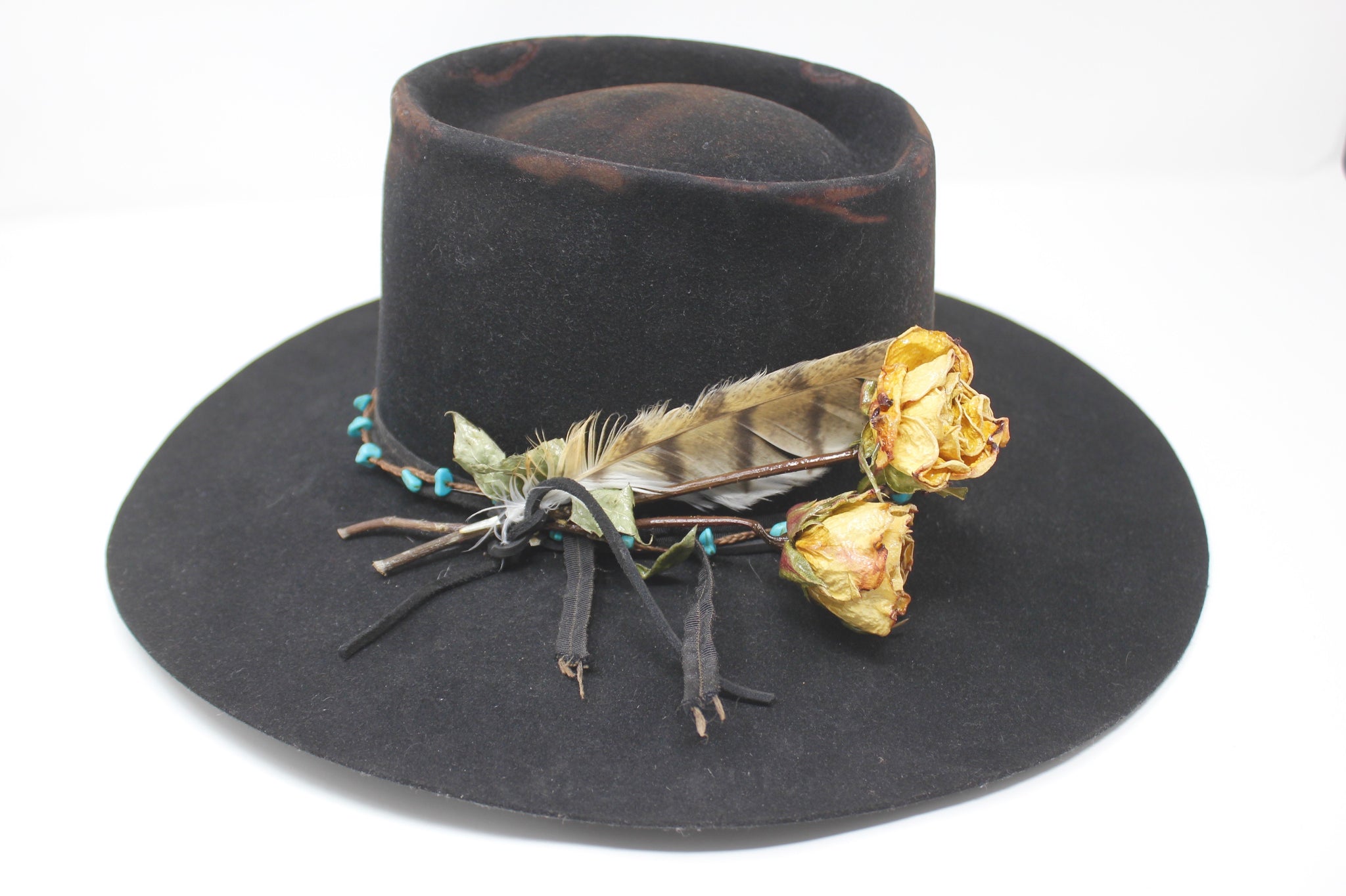 Close up view of the turquoise embellishment, and found feather detail on The Horse Thief Badlands custom Lone Hawk hat featuring a distressed telescope crown, wide flat brim, handcrafted in California.