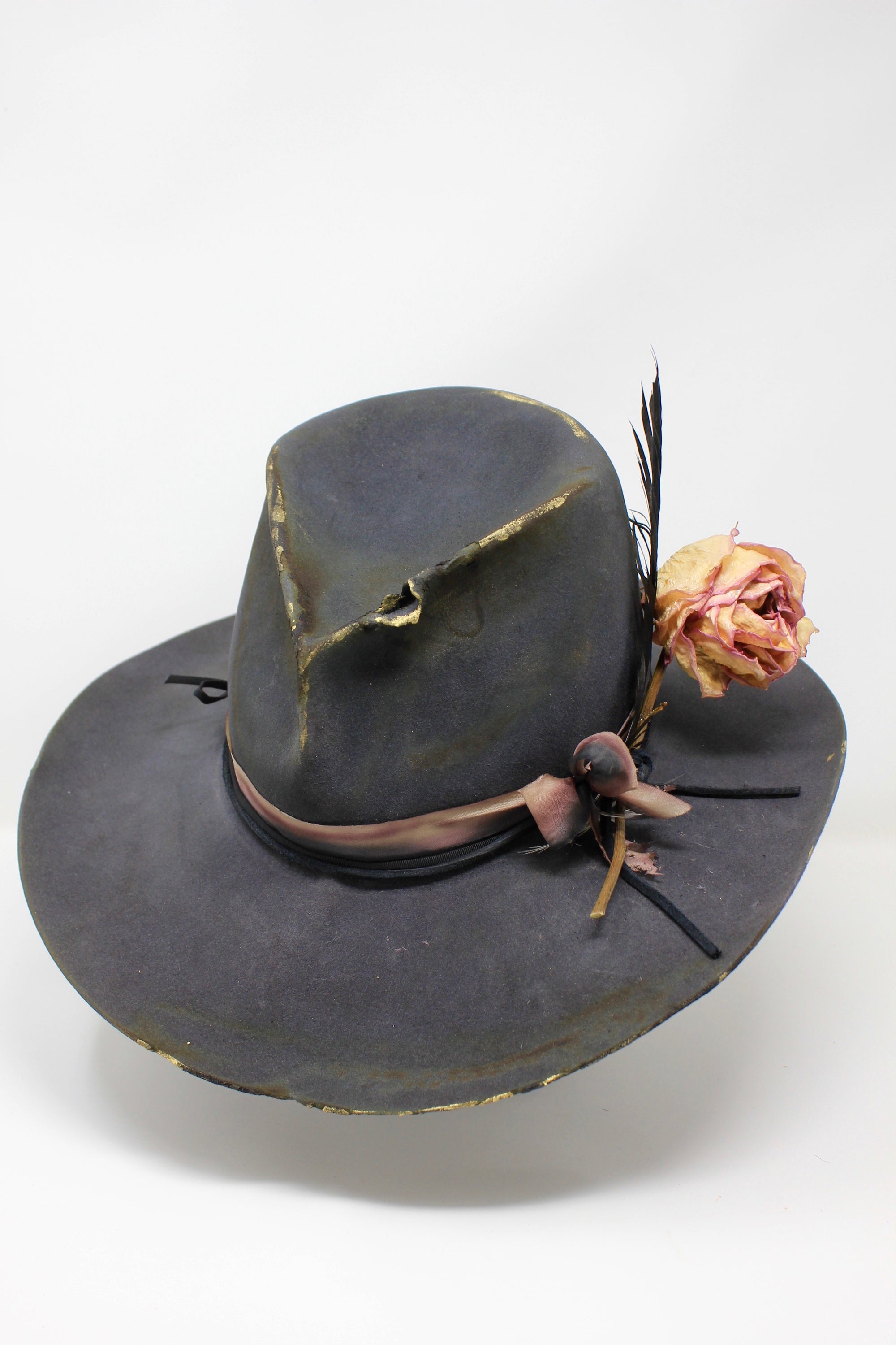 front view of The Ramblin' Rose by Lone Hawk Hats, a handmade distressed grey beaver blend hat featuring a pinched crown, silk ribbon, gold highlights, and a dried rose and feather bouquet.
