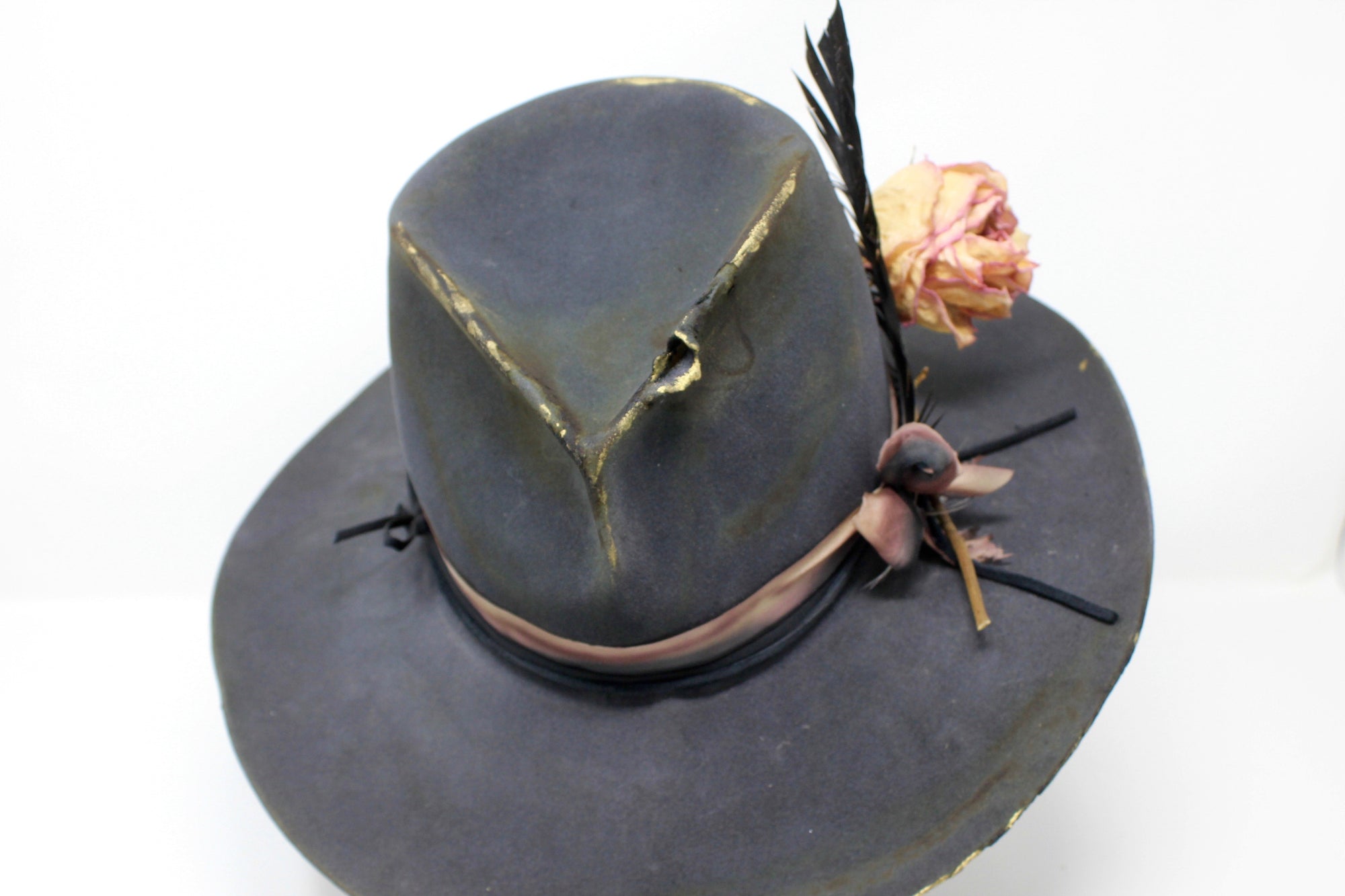 Top view of The Ramblin' Rose by Lone Hawk Hats, a handmade distressed grey beaver blend hat featuring a pinched crown, silk ribbon, gold highlights, and a dried rose and feather bouquet.