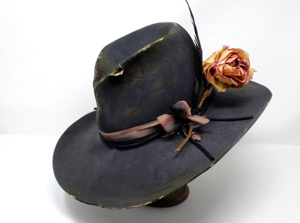 Left view of The Ramblin' Rose by Lone Hawk Hats, a one of a kind handmade distressed grey beaver blend hat featuring a pinched crown, silk ribbon, gold highlights, and a dried rose and feather bouquet.